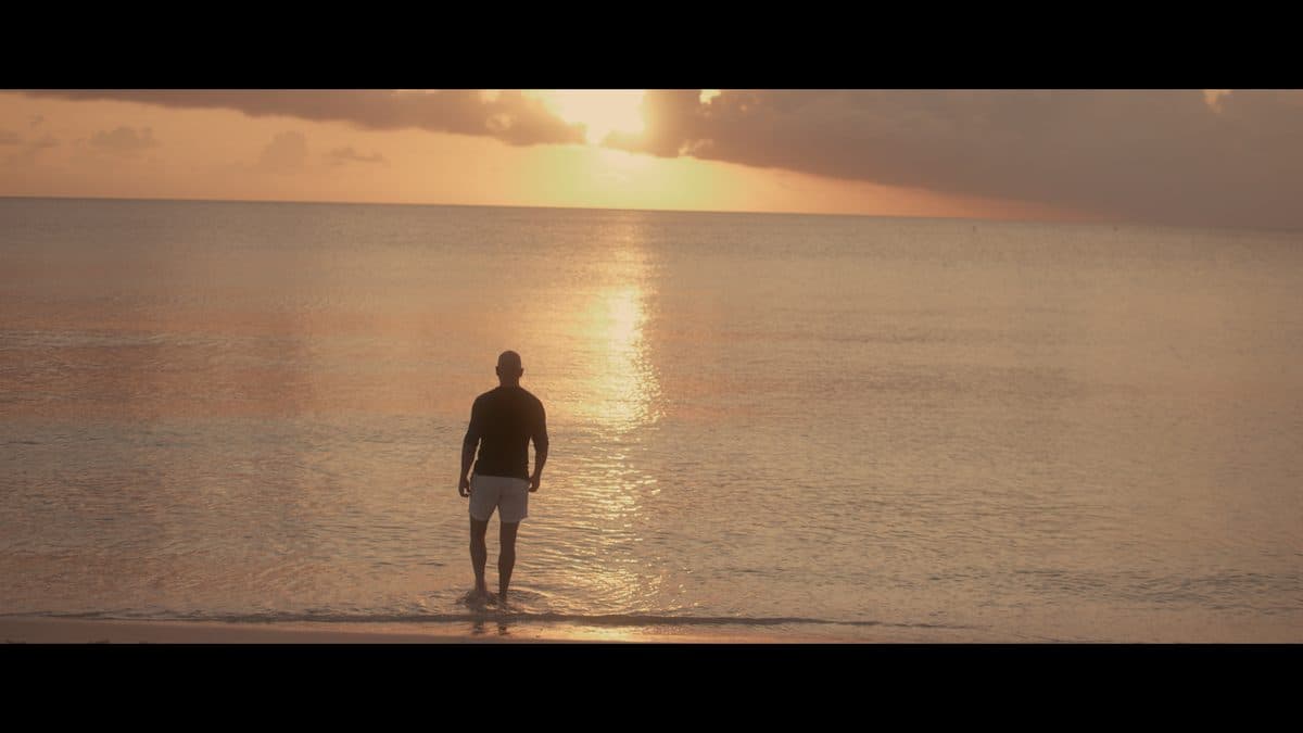 A lone figure walking into a calm sea at sunrise