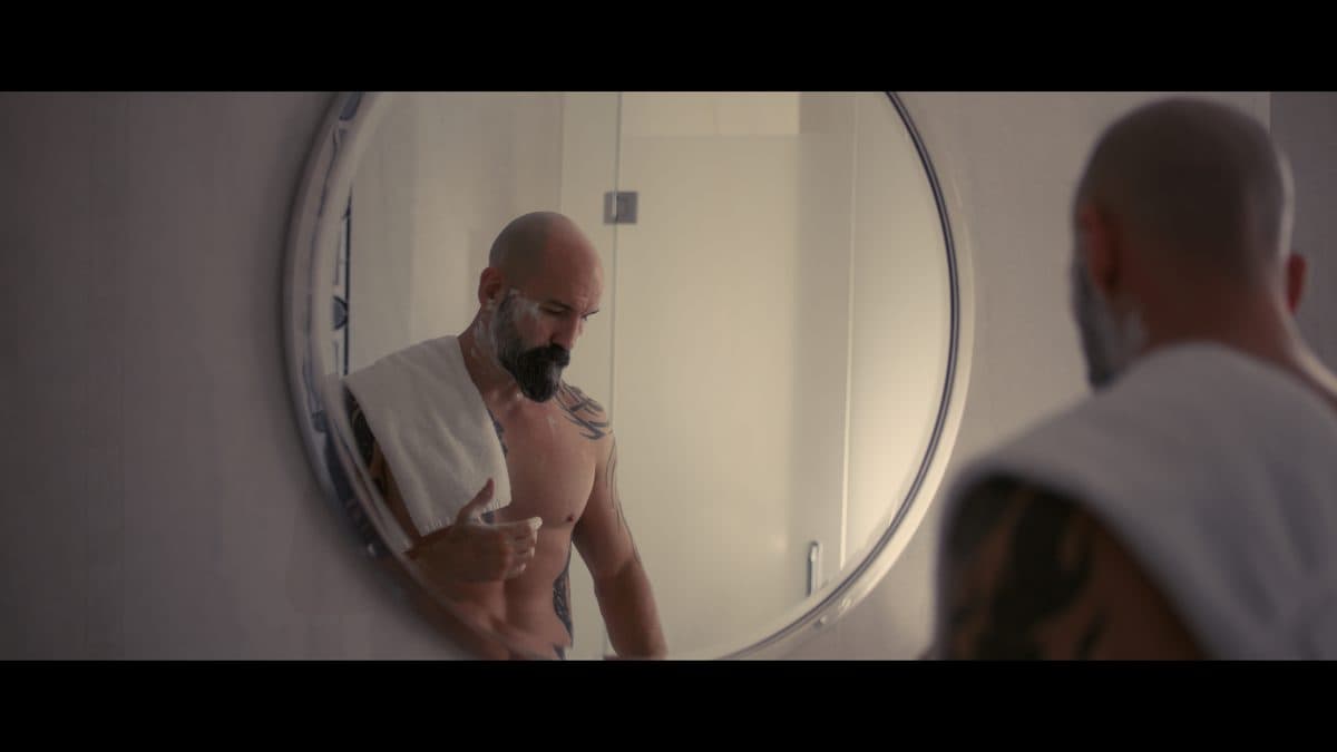 A man reflected in a round mirror with a towel over his shoulder