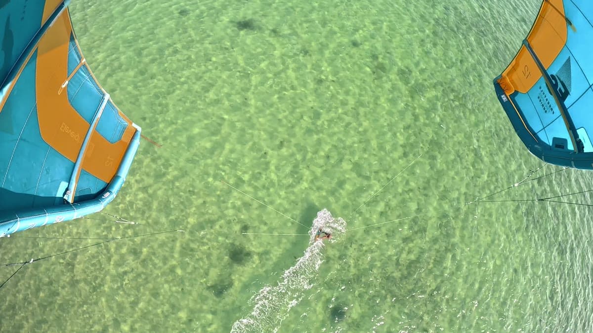 A kite surfer from above, cutting across shallow turquoise water